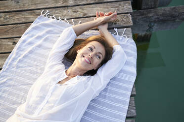 Lächelnde reife Frau auf einem Handtuch liegend auf einem Steg an einem See - PNEF02189