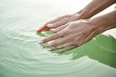 Nahaufnahme der Hände einer Frau, die das Wasser eines Sees berühren - PNEF02205