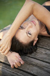 Portait of mature woman lying on a jetty at a lake - PNEF02214