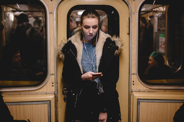 Young woman listening music on phone while traveling in subway train - CAVF65486