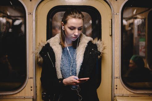 Junge Frau benutzt ihr Smartphone während der Fahrt in der U-Bahn - CAVF65487