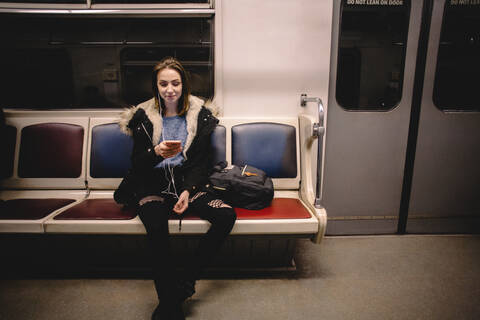 Junge glückliche Frau benutzt ihr Smartphone während der Fahrt in der U-Bahn, lizenzfreies Stockfoto