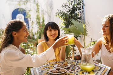 Three happy female friends meeting in a cafe clinking lemonade glasses - MPPF00128