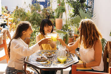 Three happy female friends meeting in a cafe clinking lemonade glasses - MPPF00130