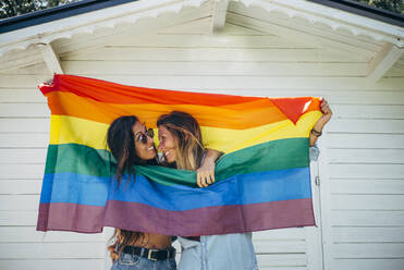 Zwei lächelnde Frauen halten eine Regenbogenflagge hoch - OCMF00810