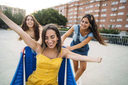 Three playful female friends with shopping cart in the city - MPPF00190