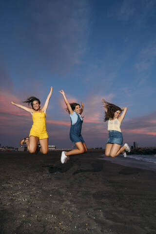 Three carefree female friends jumping on the beach at sunset stock photo