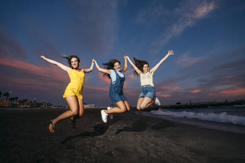Three carefree female friends jumping on the beach at sunset stock photo
