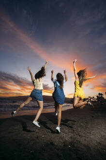 Rückansicht von drei sorglosen Freundinnen, die bei Sonnenuntergang am Strand springen - MPPF00202