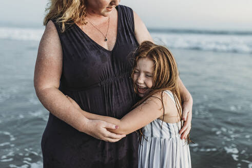 Seitenansicht einer glücklichen jungen Tochter, die ihre Mutter in der Abenddämmerung im Meer umarmt - CAVF65533