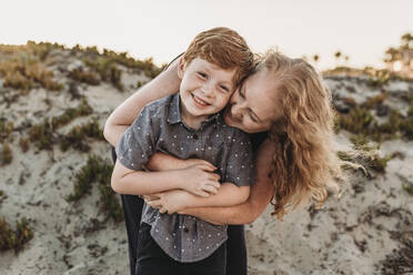 Front view of mother hugging redheaded kindergarten age son at sunset - CAVF65539