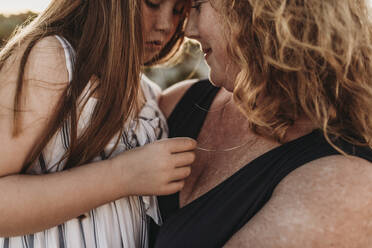 Side view of mother and redheaded elementary age daughter at sunset - CAVF65540