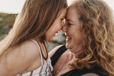 Side view of mother and redheaded elementary age daughter at sunset - CAVF65541