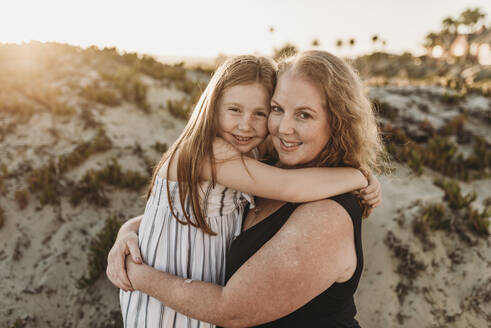 Seitenansicht von Mutter und rothaariger Tochter im Grundschulalter bei Sonnenuntergang - CAVF65542