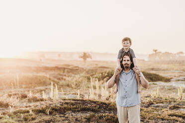 Father holding son up on shoulders while smiling at camera at beach - CAVF65545