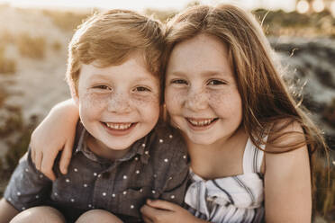 Portrait of young redheaded freckled siblings smiling during sunset - CAVF65547
