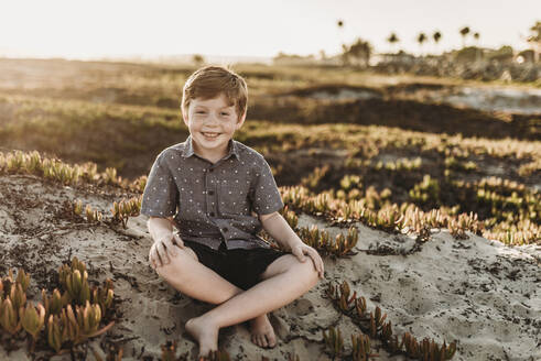 Porträt eines jungen rothaarigen Jungen mit Sommersprossen, der sitzt und lächelt - CAVF65552