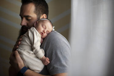 Vater umarmt schlafende neugeborene Tochter an der Schulter zu Hause - CAVF65564