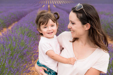 Glückliche Mutter und Tochter beim Spaziergang zwischen Lavendelfeldern im Sommer - CAVF65570