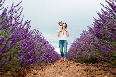 Mother and daughter walking among lavender fields in the summer - CAVF65573