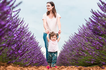 Happy mother and daughter walking among lavender fields in the summer - CAVF65576