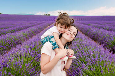 Happy woman and little girl walking among lavender fields in summer - CAVF65579