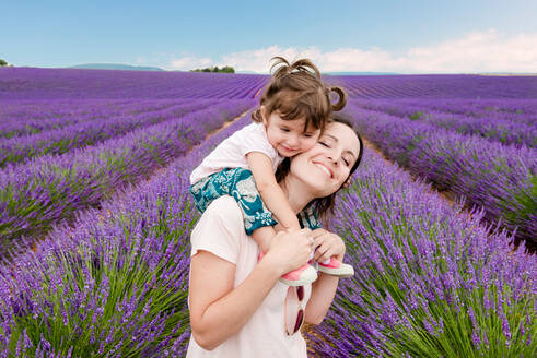 Glückliche Frau und kleines Mädchen spazieren zwischen Lavendelfeldern im Sommer - CAVF65579