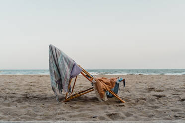 Spanien, Provinz Barcelona, El Garraf, Strandtücher hängen am Liegestuhl links am sandigen Küstenstrand in der Abenddämmerung - AFVF04061