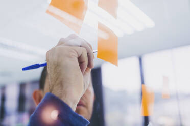 Mature businessman writing on sticky notes at glass pane in office - CAVF65589