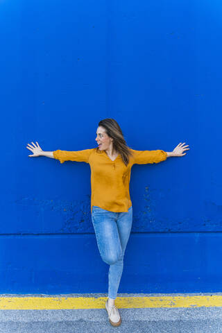 Junge überraschte Frau lehnt an blauer Wand, lizenzfreies Stockfoto