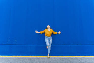 Young screaming woman leaning on blue wall - AFVF04064