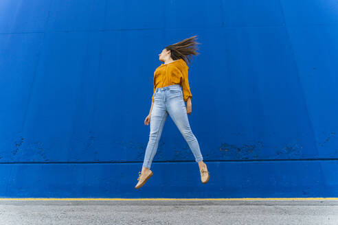 Junge Frau springt vor einer blauen Wand - AFVF04065