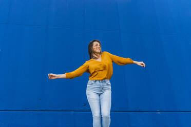 Young dancing woman in front of a blue wall - AFVF04066