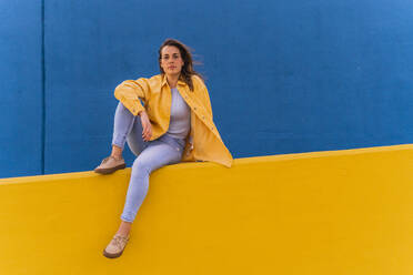 Young woman sitting on an yellow wall - AFVF04071