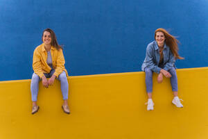 Junge lächelnde Frauen, die an einer orangefarbenen Wand sitzen - AFVF04073
