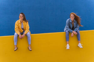 Young smiling women sitting on an orange wall - AFVF04073