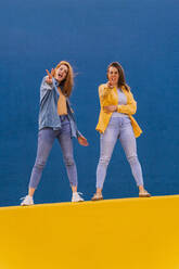 Young women standing on an orange wall and showing peace sign - AFVF04077