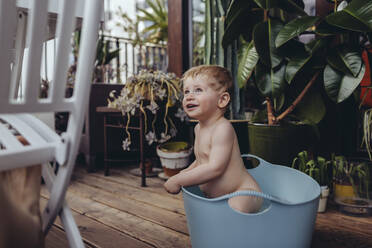 Ein kleiner Junge sitzt in der Babywanne auf dem Balkon und versucht aufzustehen - MFF04897