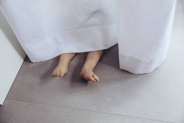 Beine und Füße eines kleinen Jungen, der sich hinter einem Vorhang versteckt - MFF04910