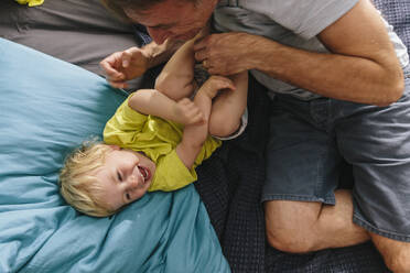 Father cuddling and tickling son on bed - MFF04930