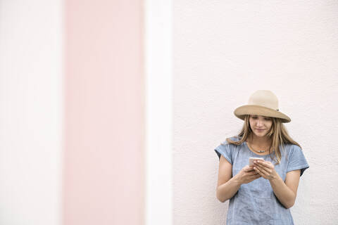 Frau steht an einer Wand und benutzt ein Smartphone, lizenzfreies Stockfoto