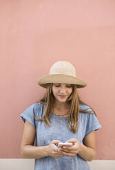 Woman standing at a pink wall using smartphone - AHSF00934