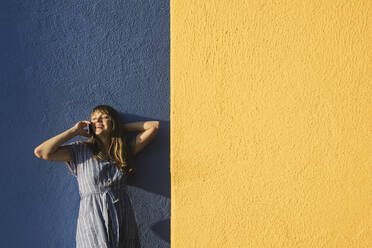 Glückliche Frau am Telefon vor gelben und blauen Wänden - AHSF00949