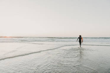 Rear view of running surfer on the beach at sunset, Costa Nova, Portugal - AHSF00956