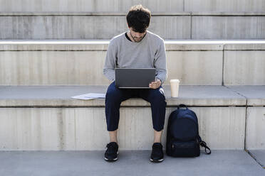 Mann sitzt auf einer Außentreppe und benutzt einen Laptop - GIOF07235