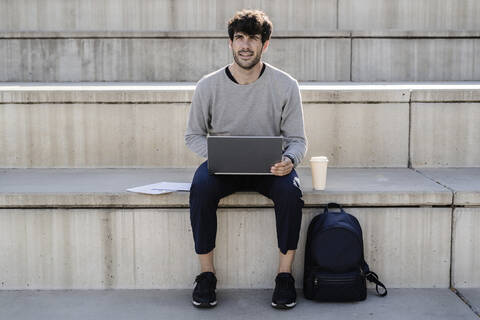 Mann sitzt auf einer Außentreppe und benutzt einen Laptop, lizenzfreies Stockfoto