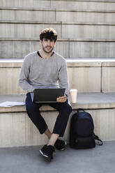 Mann sitzt auf einer Außentreppe und benutzt einen Laptop - GIOF07242