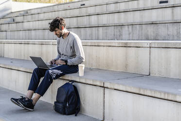 Man sitting on outdoor stairs using laptop - GIOF07248