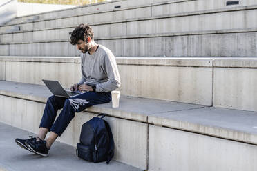 Mann sitzt auf einer Außentreppe und benutzt einen Laptop - GIOF07248