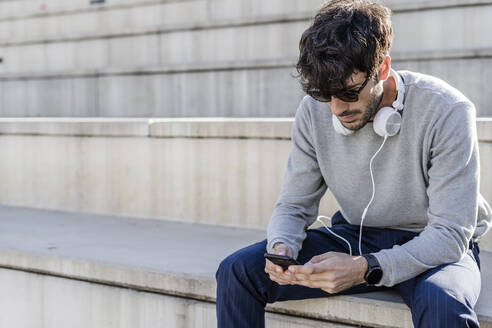 Mann sitzt auf einer Außentreppe und benutzt sein Smartphone - GIOF07250